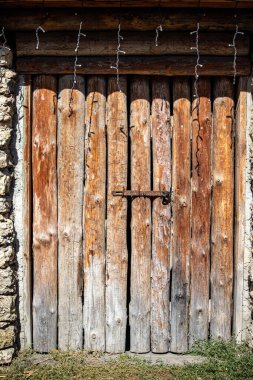 The door is old and has a rusty lock. It is made of wood and has a cross on it