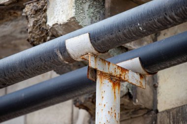 A rusty pipe is attached to a metal pole. The pipe is black and the pole is white