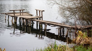 Masası ve tezgahı olan ahşap bir iskele suyun içinde. Rıhtım eski ve kırsal bir havası var. Su sakin ve huzurlu.