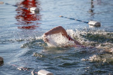 Suda bir yüzücü var ve su mavi. Yüzücü kırmızı bir gömlek giyiyor.