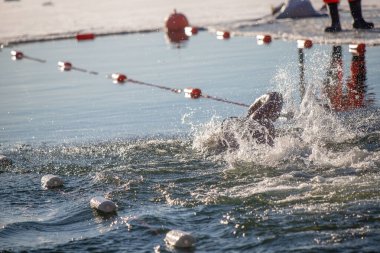 Suda kırmızı bir şamandırayla havuzda yüzen bir adam var. Su dalgalı ve adam etrafa sıçrıyor.