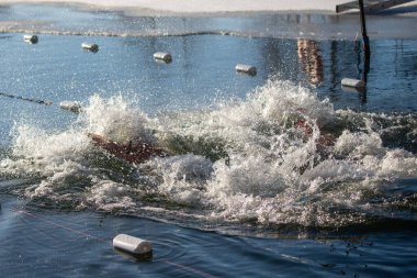 Bir adam suda yüzüyor ve su sıçrıyor. Su mavi ve adam kırmızı bir gömlek giyiyor.