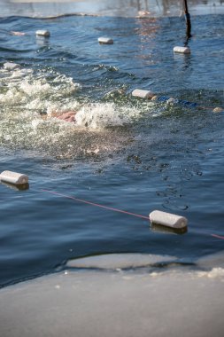 Arka planda kırmızı bir çizgi olan bir kişi suda yüzüyor. Su soğuk ve kişi mayo giyiyor.