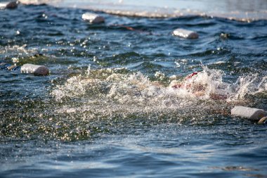Bir yüzücü suda ve etrafa su sıçratıyor. Su sakin ve berrak. Yüzücü kırmızı bir mayo giyiyor.