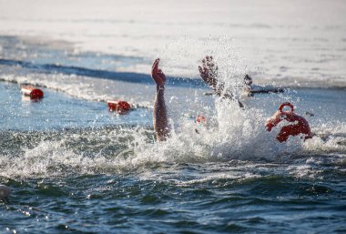 Bir adam okyanusta yüzüyor ve suya çarpmak üzere. Su soğuk ve adam kırmızı bir can yeleği giyiyor.