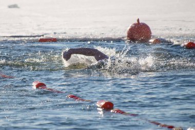 Suda bir yüzücü var ve suda kırmızı bir şamandıra var. Su sakin ve berrak.