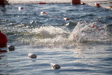 Bir yüzücü suyun içindedir, etrafa su sıçratır ve dalgalanmalar yaratır. Su sakin ve berrak, yakınlarda birkaç şamandıra yüzüyor. Sahne huzurlu ve rahatlatıcı, yüzücü suyun tadını çıkarıyor.