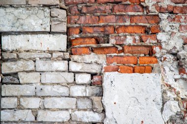 A brick wall with a white brick in the middle. The wall is crumbling and has a lot of cracks