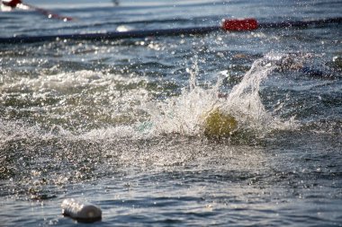 Bir yüzücü suda ve etrafa su sıçratıyor. Su bulanık ve içinde plastik şişeler yüzüyor.