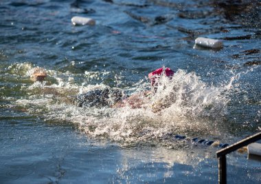 Kırmızı şapkalı bir adam havuzda yüzüyor. O yüzerken su etrafa sıçrıyor.