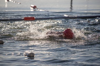 Kırmızı şapkalı ve kırmızı şamandıralı bir yüzücü suyun içinde. Su sakin ve berrak.