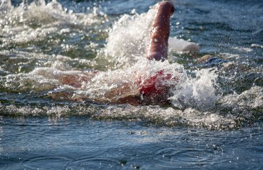 Suda bir yüzücü var ve su onun etrafına sıçrıyor. Sahne enerjik ve aktiftir