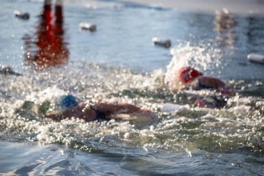 İki yüzücü suda, biri mavi bir başlık takıyor. Su sıçrıyor ve yüzücüler oradan geçiyor.