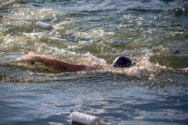 Siyah şapkalı bir adam okyanusta yüzüyor. Su dalgalı ve adam akıntıya karşı yüzüyor.