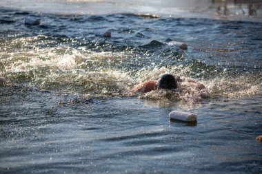 Bir adam okyanusta yüzüyor ve su sıçrıyor. Su dalgalı ve adam ayakta kalmak için mücadele ediyor.