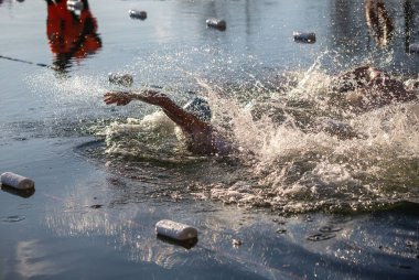 Bir adam etrafında bir sürü plastik şişeyle havuzda yüzüyor. Su bulanık ve şişeler havuzun her tarafına saçılmış.