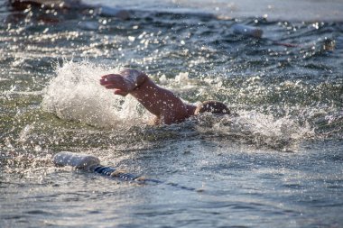 Bir adam elinde beyaz bir şamandırayla okyanusta yüzüyor. Su dalgalı ve adam etrafa sıçrıyor.