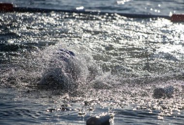 Bir adam okyanusta yüzüyor ve su sıçrıyor. Su sakin ve gökyüzü berrak.