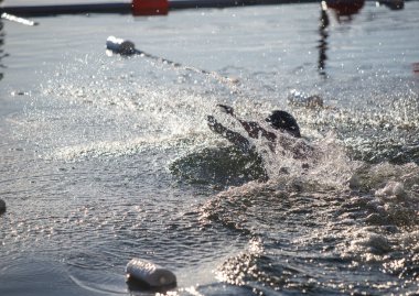 Suda beyaz bir şamandırayla havuzda yüzen bir adam var. Su sakin ve adam etrafa sıçrıyor.