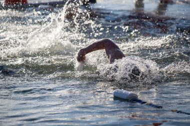 Suda bir yüzücü var ve su onun etrafına sıçrıyor. Sahne enerjik ve aktiftir