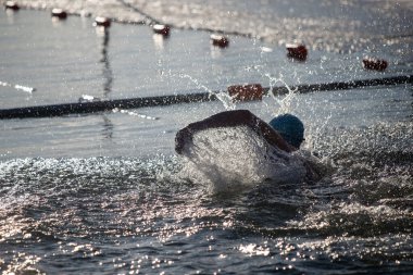 Bir yüzücü suda, su sıçratıyor ve dalgalar yaratıyor. Su sakin ve berrak ve güneş ışıl ışıl parlıyor. Sahne huzurlu ve rahatlatıcı, ve yüzücü suyun tadını çıkarıyor gibi görünüyor.