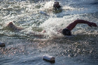 Bir adam elinde bir şişeyle okyanusta yüzüyor. Şişe beyaz ve üzerinde etiket var.