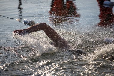 Bir yüzücü suyun içindedir, etrafa su sıçratır ve dalgalanmalar yaratır. Su sakin ve berrak, ve yüzücü siyah bir mayo giyiyor.
