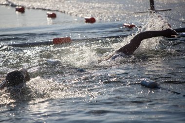 Bir adam elinde bir şişeyle havuzda yüzüyor. Su sıçrıyor ve adam sıçrıyor.