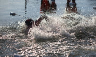 Bir adam elinde bir sopayla suda yüzüyor. Su sıçrıyor ve adam büyük bir sıçrama yapıyor.