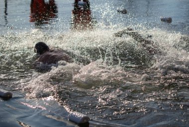 Bir adam diğer insanlarla bir havuzda yüzüyor. Su sıçrıyor ve adam su sıçrıyor.