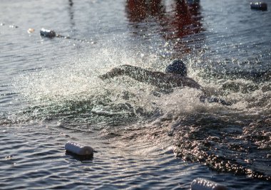 Yakınlarda bir şişeyle suda yüzen bir adam var. Su bulanık ve etrafta bir sürü plastik şişe yüzüyor.