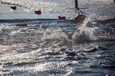 Suda kırmızı bir şamandırayla okyanusta yüzen bir adam var. Su dalgalı ve adam su sıçratıyor.