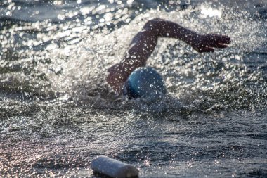 Bir yüzücü suda, mavi beyaz bir yüzme şapkası takıyor. Su sıçrıyor ve yüzücü su sıçratıyor.