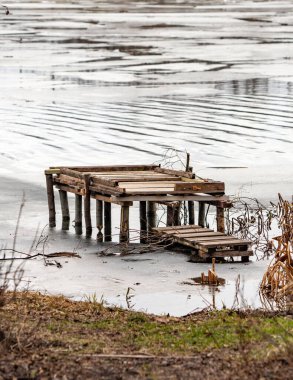 A wooden dock is floating in the water. The dock is old and has been abandoned. The water is calm and still