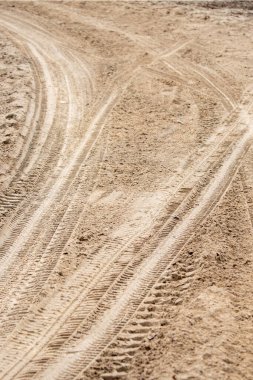 A dirt road with tire tracks in the sand. The tire tracks are in a zigzag pattern, and the road appears to be worn down and dusty. Scene is somewhat desolate and abandoned