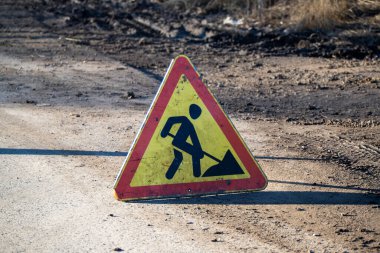 Elinde kürek olan bir adam ve kırmızı ve sarı işareti olan bir üçgen.