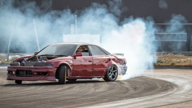 Kırmızı bir araba egzozundan duman çıkan bir pistte gidiyor. Araba hızlı gidiyor ve o bir yarışta.