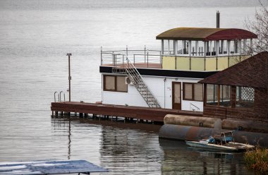 Kırmızı çatılı bir evin yanına bir tekne yanaştı. Su sakin ve gökyüzü bulutlu.