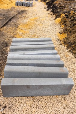 Yerde bir yığın gri tuğla, toprak yığınının yanında. Tuğlalar üst üste dizilmiş ve toprak etrafa saçılmış. Sahne inşaat ya da yenileme hissi veriyor.