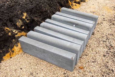 A pile of bricks is laying on the ground. The bricks are grey and are stacked in a row