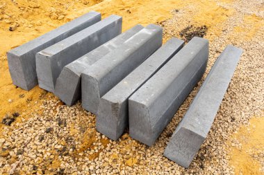 Bir kaç tanesi ortadan ikiye bölünmüş gri tuğla yığını. Tuğlalar üst üste istiflenmiş ve kumlu bir yüzeye uzanıyorlar.