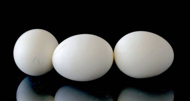 Three eggs are sitting on a black surface. The eggs are white and appear to be identical in size