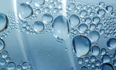 Görüntü, üzerinde su damlaları olan bir bardak suyun görüntüsü. Damlacıklar küçük ve dağınık, hareket ve akıcılık hissi yaratıyorlar.