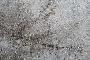 A grey and white surface with a lot of gravel and dirt. The surface is rough and uneven