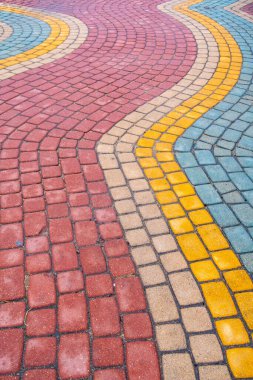 A brick walkway with a colorful pattern. The colors are red, yellow, and blue. The walkway is curved and has a unique design