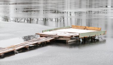 Suda bir ahşap iskele yüzüyor. Rıhtım karla kaplı ve o bakımsız. Su sakin ve hareketsiz, arka planda gri bir gökyüzü var. Yalnızlık ve sessizlik kavramı