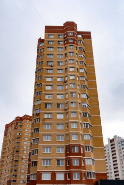 Bir sürü penceresi ve beyaz çatısı olan uzun kahverengi bir bina. Bina diğer binalarla çevrili.