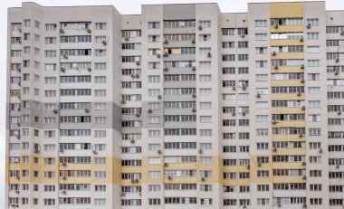 Bir sürü penceresi ve kliması olan büyük bir apartman. Bina çoğunlukla beyaz ve sarı ve kahverengi renkli.