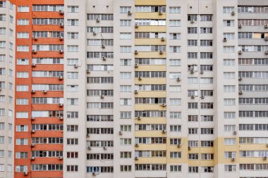 A large building with many windows and air conditioners. The building is mostly white and orange