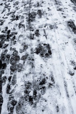 Araçların lastik izleri olan karlı bir yol. Yol karla kaplı ve araçların ve kamyonların tekerlek izleri var. İzler yol boyunca yayılmış, hareket ve hareketlilik hissi yaratıyor.